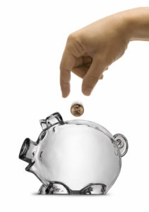 male hand dropping a coin into a clear piggy bank full of coins.